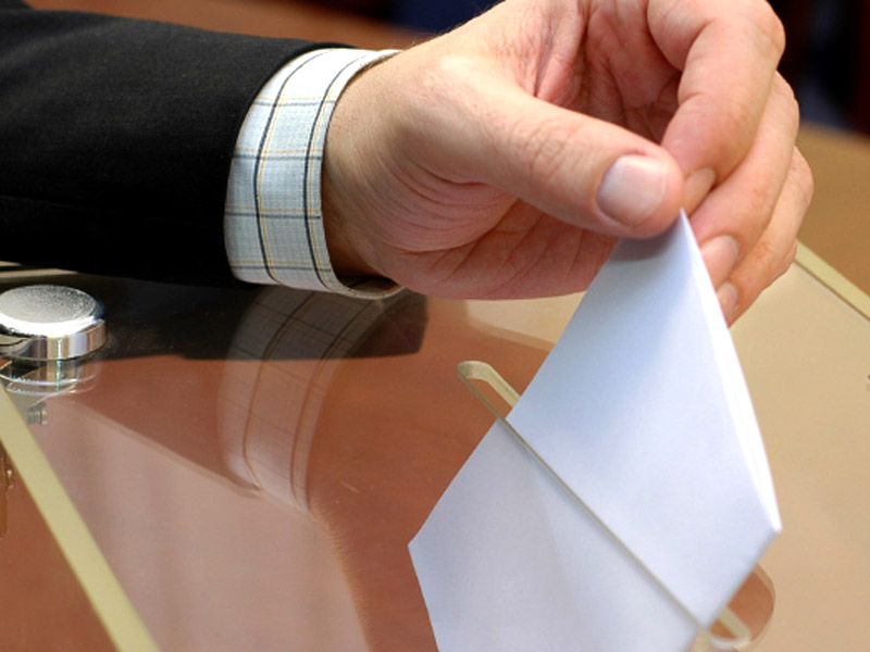 Person, die ein Kuvert in die Wahlbox wirft